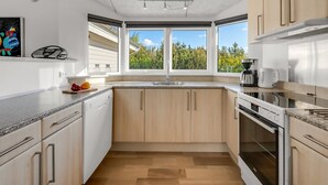 Eine moderne Küche mit Fenster, Holzschränken, einem Geschirrspüler und einem Backofen.