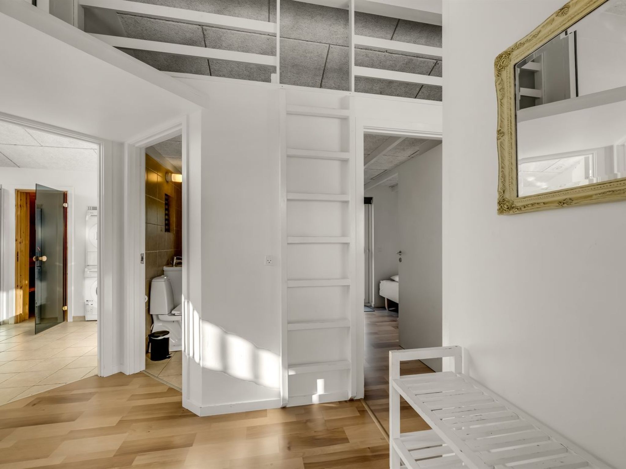 Een modern interieur met een houten vloer, witte muren, een grote witte deur en een spiegel met een sierlijk lijstwerk.
