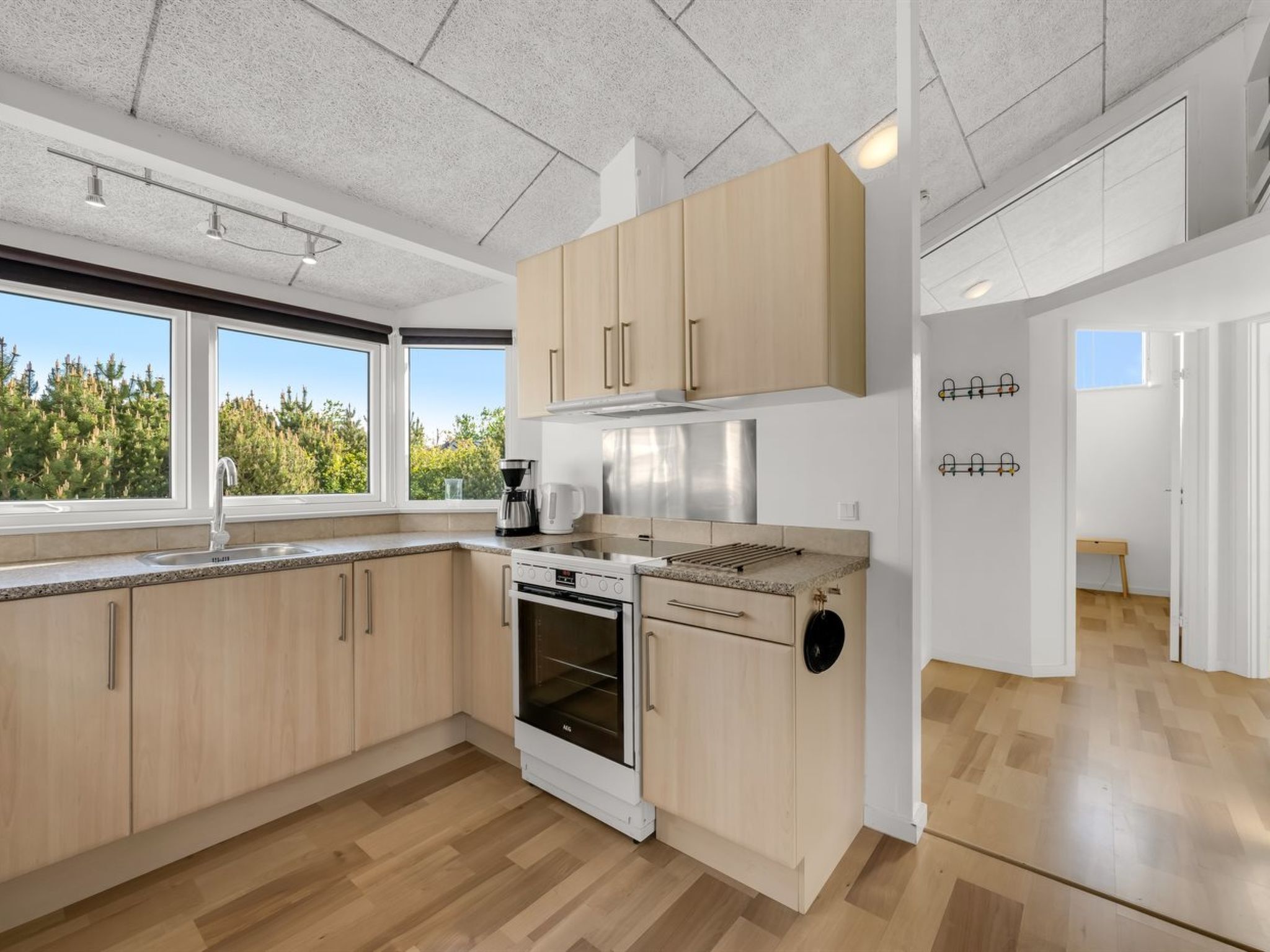 A modern kitchen with wooden cabinets, a stainless steel range, and a window with a view of trees.