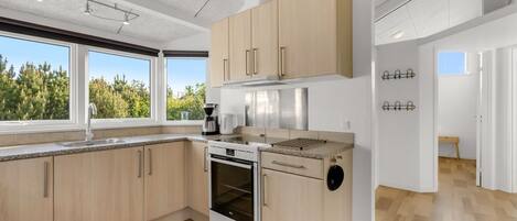 A modern kitchen with wooden cabinets, a stainless steel range, and a window with a view of trees.