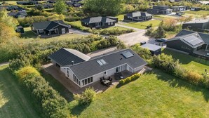 Ein Wohngebiet mit mehreren Häusern, einige mit Solaranlagen, umgeben von Grünflächen und offenen Feldern.
