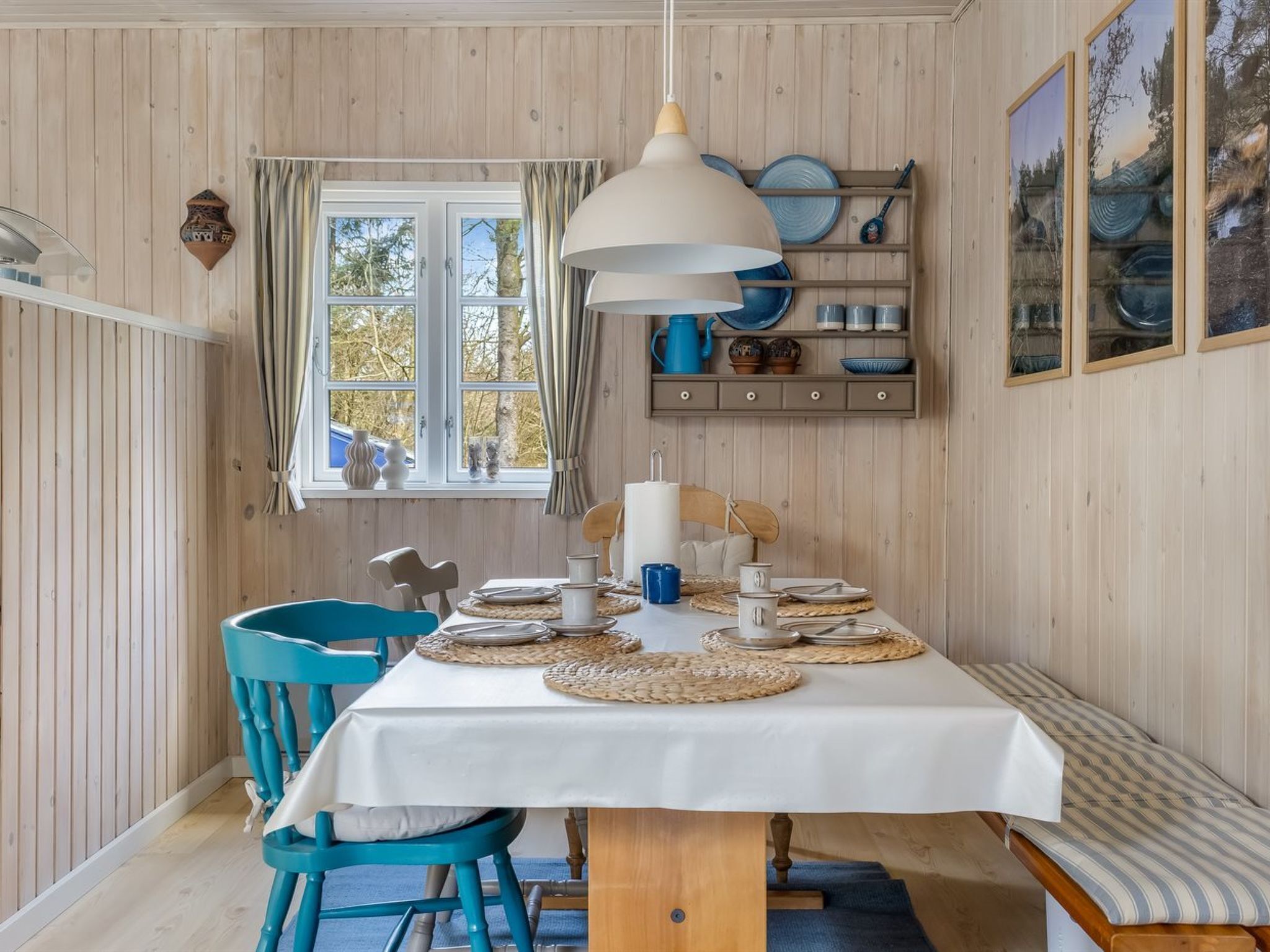 Comedor con mesa dispuesta para dos, una lámpara colgante y una ventana con cortinas.