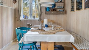 A dining area with a table set for two, a hanging pendant light, and a window with curtains.