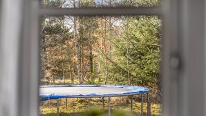 A window view of a trampoline in a yard with trees.