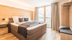 A bedroom with a bed, a bench, a wooden wall, and a window with curtains.