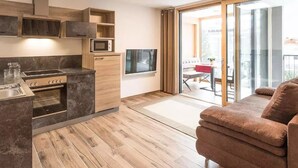 A modern kitchen with built-in appliances, a dining area with a red table, and a sliding glass door to a balcony.