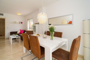Un espace de salle à manger moderne avec une table blanche, des chaises marron, un luminaire suspendu et un vase rempli de fleurs.