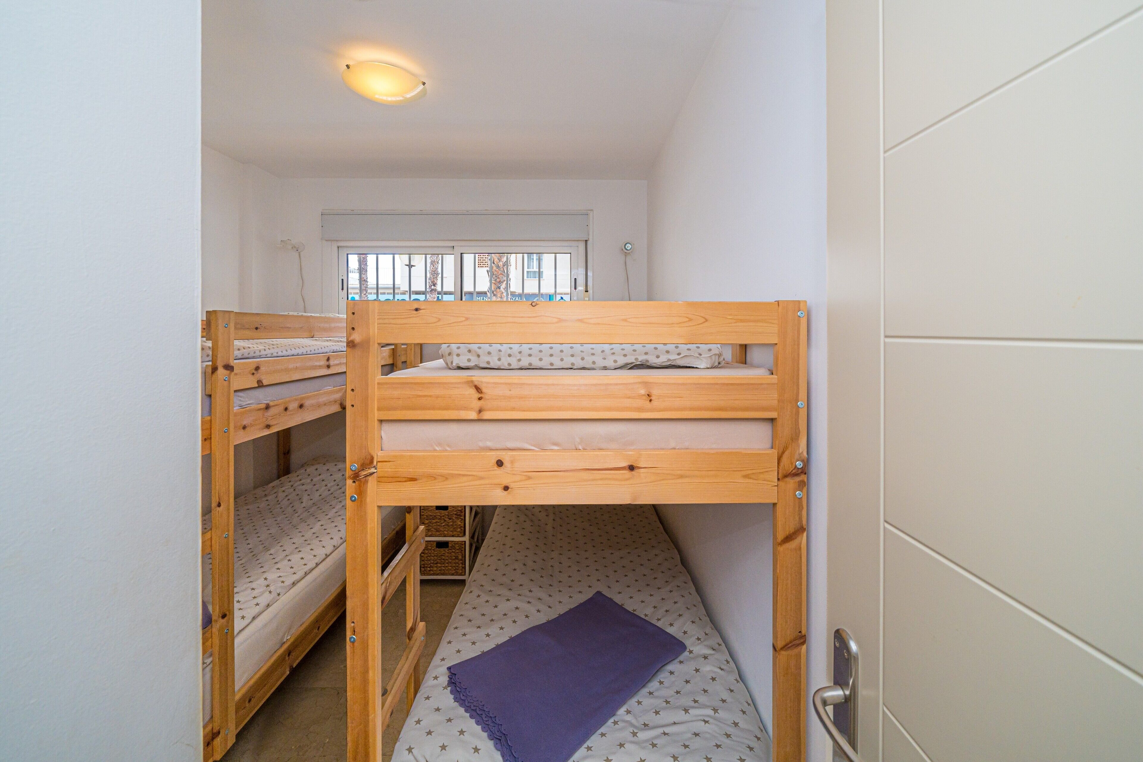 Une chambre de dortoir avec des lits superposés, une fenêtre avec des stores et une porte.