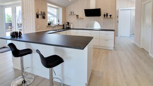 A modern kitchen with a large island, bar stools, wooden paneling, and a flat-screen TV.