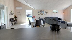 A modern living room with a dining area, featuring a large gray sofa, a dining table with chairs, and a kitchen island with a black decorative piece.