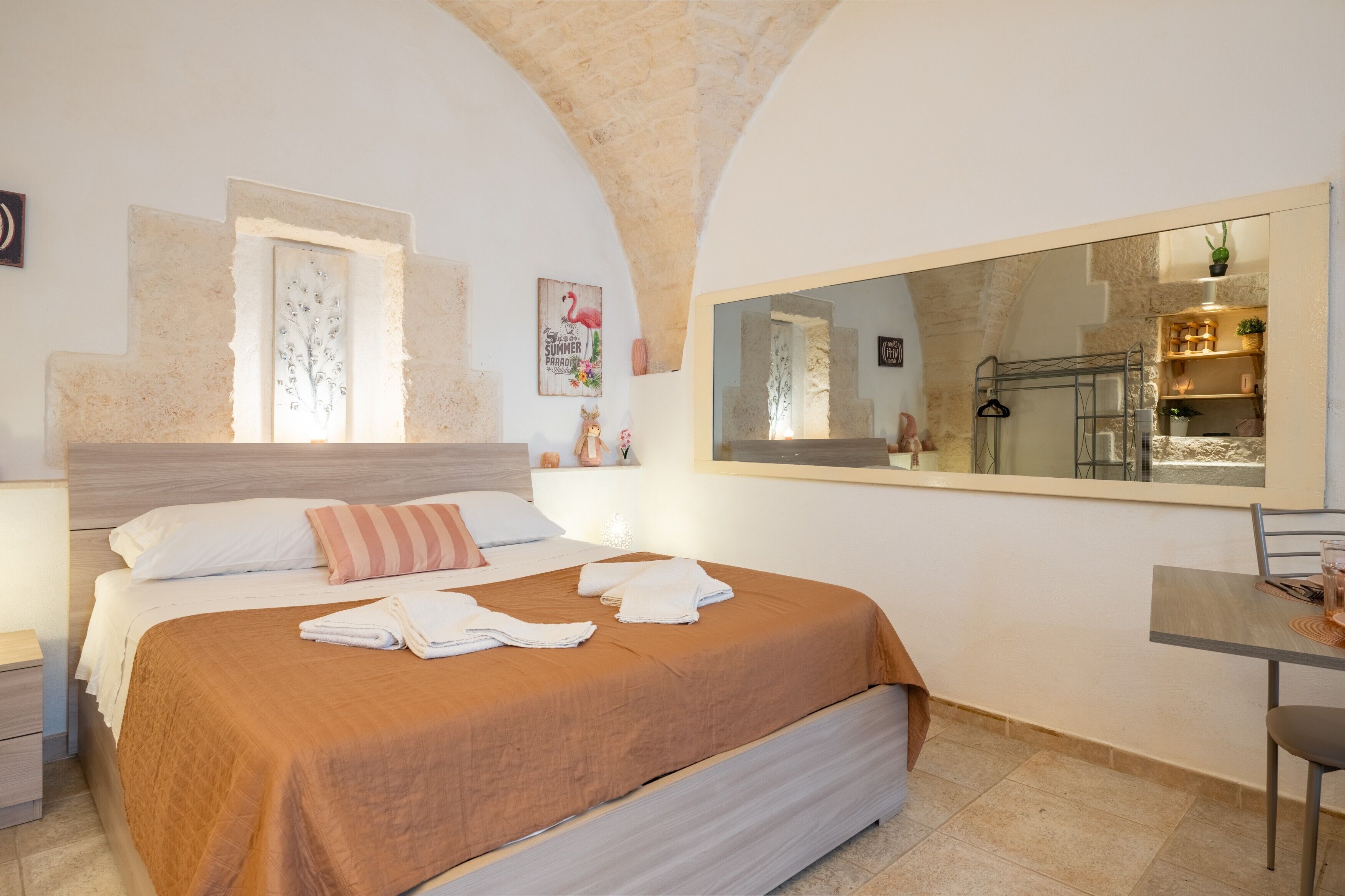 Una camera d'albergo con un letto, una scrivania, una sedia, uno specchio grande e vista sulla cucina.