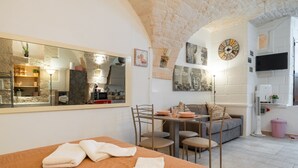 A hotel room with a bed, a dining table, a sofa, a mirror, artwork, a clock, and a television. - Holiday Home 'Pietrarosa Loft' with Wi-Fi (Ostuni)