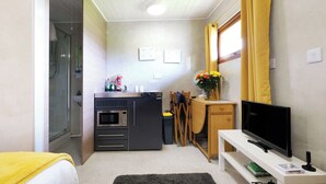 Quarto de hotel compacto com cozinha compacta, uma cama, televisão e chuveiro.