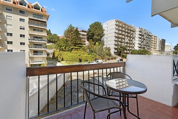 A balcony with a table and chairs, overlooking a residential area with multi-story buildings and greenery. - Holiday Home 'Estoril Art and Surf' with Balcony, Wi-Fi and Air Conditioning (Estoril)