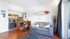 Un espacio habitable compacto con kitchenette, sofá, zona de comedor y un amplio ventanal.