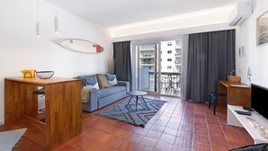 Una sala de estar moderna con un sofá, una mesa de centro, un televisor y un balcón con vistas a la ciudad.