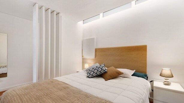 Un dormitorio con cama, mesita de noche, lámpara y ventana con persianas.