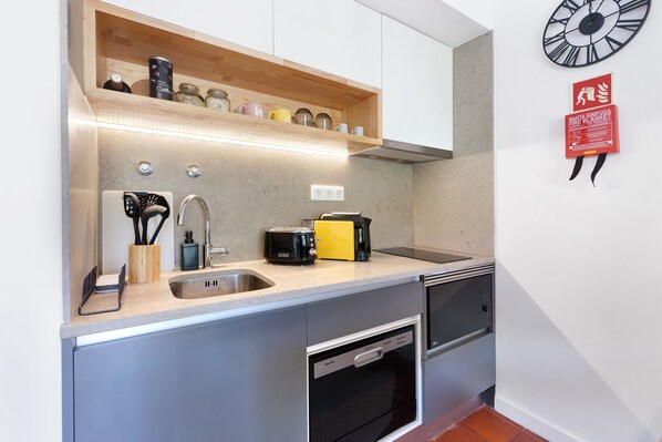 A kitchen with a stainless steel sink, a toaster, a coffee maker, and a fire blanket on the wall.