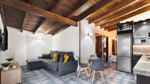 A modern kitchen with a built-in oven and refrigerator, a dining area with a table and chairs, a gray sofa with yellow cushions, and a wooden ceiling. - Vacation Home "Ático Miranda" with Jacuzzi, Views of El Teide & Wi-Fi (Icod de los Vinos)