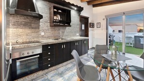 A modern kitchen with granite countertops, a built-in stove, and a dining area with a glass table and chairs. - Vacation Home "Ático Miranda" with Jacuzzi, Views of El Teide & Wi-Fi (Icod de los Vinos)