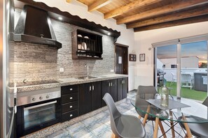 Une cuisine moderne dotée de plans de travail en granit, d’une cuisinière encastrée et d’un coin repas avec une table et des chaises en verre.