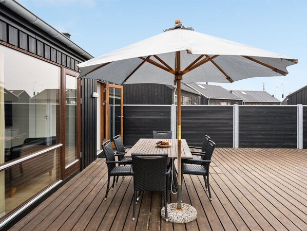 Une terrasse en bois avec une table et des chaises, protégée par un grand parasol.