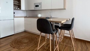 Una cocina moderna con armarios blancos, un microondas y un lavabo. Hay dos sillas negras y una mesa de comedor de madera.