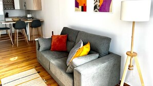 Una sala de estar moderna con un sofá gris, una zona de comedor con una cocina al fondo y una lámpara de pie.