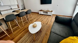 A modern living space with a kitchen, dining area, and a TV mounted on the wall. - Vacation Home "Amber L5" with Sea View & Wi-Fi (Armeñime)