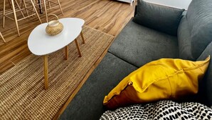 A modern living room with a sofa, a dining table with chairs, a TV mounted on the wall, and a small white side table. - Vacation Home "Amber L5" with Sea View & Wi-Fi (Armeñime)