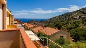 Un pueblo costero con edificios de tejados de terracota, un cielo azul despejado y vista al mar.