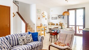 Una sala de estar con un sofá a rayas, una mesa de comedor con sillas, una silla de mimbre y una escalera.