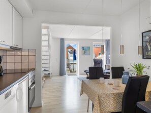 Una cocina moderna con armarios blancos, encimera oscura y zona de comedor con mesa y sillas.