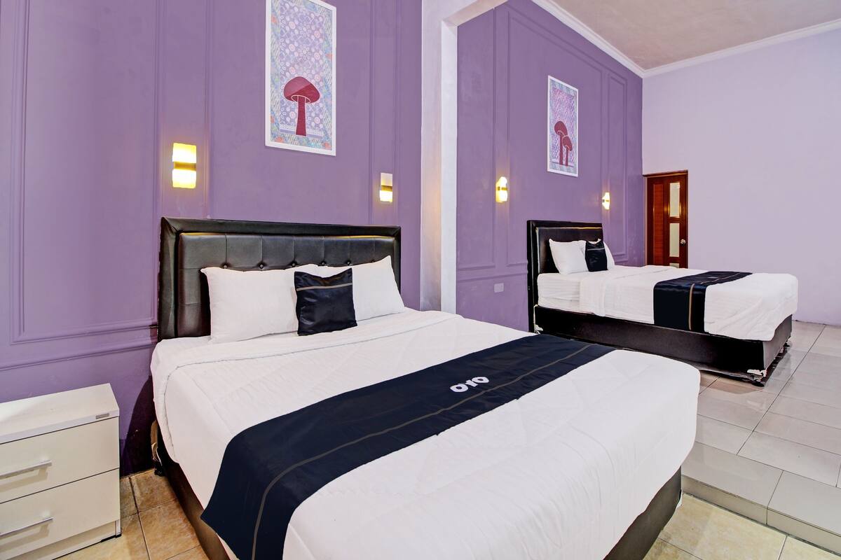 Habitación de hotel con dos camas, un escritorio blanco y paredes moradas.