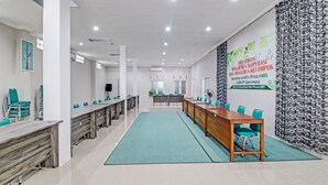 Un salón de conferencias con una mesa larga, sillas color turquesa y un papel tapiz estampado.
