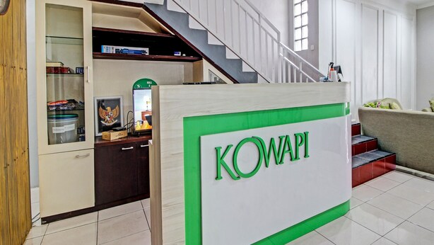 Un área de recepción con un cartel que dice "KOWAPI", una escalera y un armario de madera con puertas de vidrio.