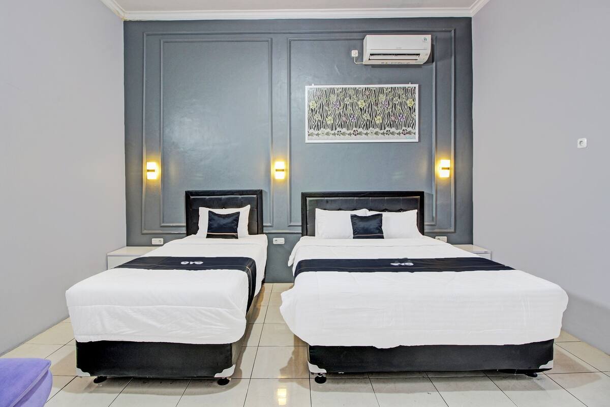 Una habitación de hotel con dos camas, una pared de acento gris y una obra enmarcada sobre las camas.