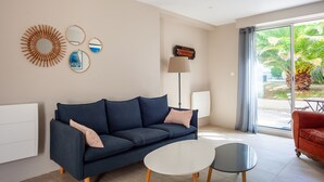 Sala de estar com um sofá azul escuro, uma mesa de centro branca, um abajur e vista para um jardim através de uma grande janela.