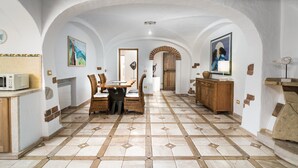 Una cocina amplia con comedor, que cuenta con piso de baldosas, mobiliario de madera y paredes blancas con arcos.