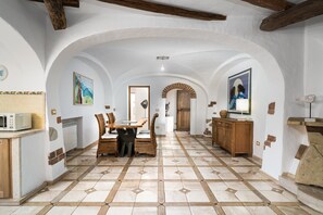 A spacious kitchen with a dining area, featuring a tiled floor, wooden furniture, and white walls with arches.