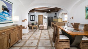 Una cocina amplia con techo abovedado, un comedor con sillas de mimbre y una sala de estar con sofá y mesita de centro.