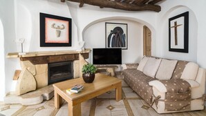 Una sala de estar con chimenea, sofá, mesa de centro, televisor y obras de arte en las paredes.