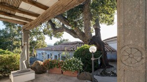 Un espacio al aire libre cubierto con un banco de piedra, un árbol grande y un edificio con techo de tejas al fondo.