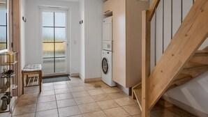 Un espacio habitable compacto con lavadora, un banco, una puerta con paneles de vidrio esmerilado y una escalera.
