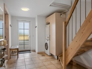 A compact living space with a washing machine, a bench, a door with frosted glass panels, and a staircase.