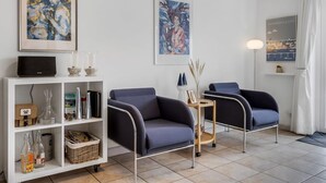 Una sala de estar moderna con dos sillones azul oscuro, una estantería blanca con diversos objetos y dos obras de arte enmarcadas en la pared.