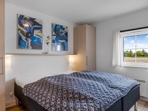Une chambre à coucher avec un lit, deux tableaux abstraits, une fenêtre donnant sur un paysage et un radiateur.