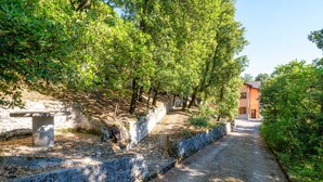 A gravel path flanked by stone walls and trees, leading to a building with a red facade. - Villa Marta Apartment: Nature, Tranquility, and Authentic Umbrian Charm (Spoleto)