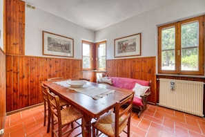 A dining area with a wooden table and chairs, a red sofa, and two framed pictures on the walls.