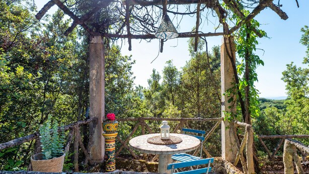 A rustic outdoor seating area with a round table and blue chairs, surrounded by trees and a view of the landscape. - Villa Marta Apartment: Nature, Tranquility, and Authentic Umbrian Charm (Spoleto)